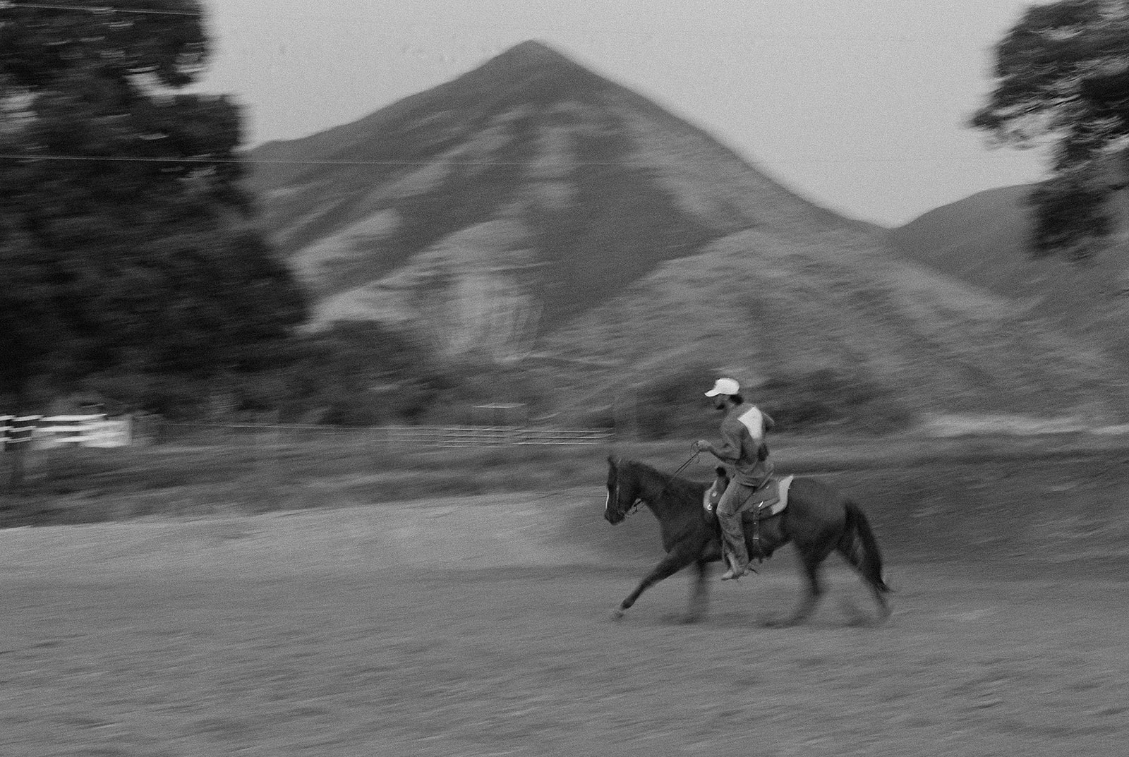 Black and white motion-blur shot of a cowboy galloping past the mountains