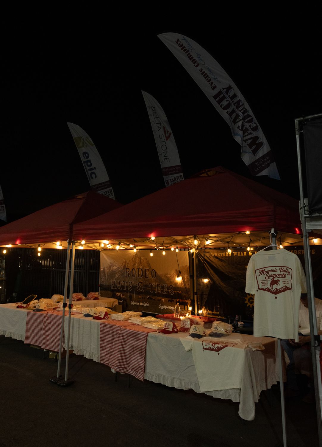 The Loud Face tent lit up at night with hats and tees laid out for the rodeo crowd