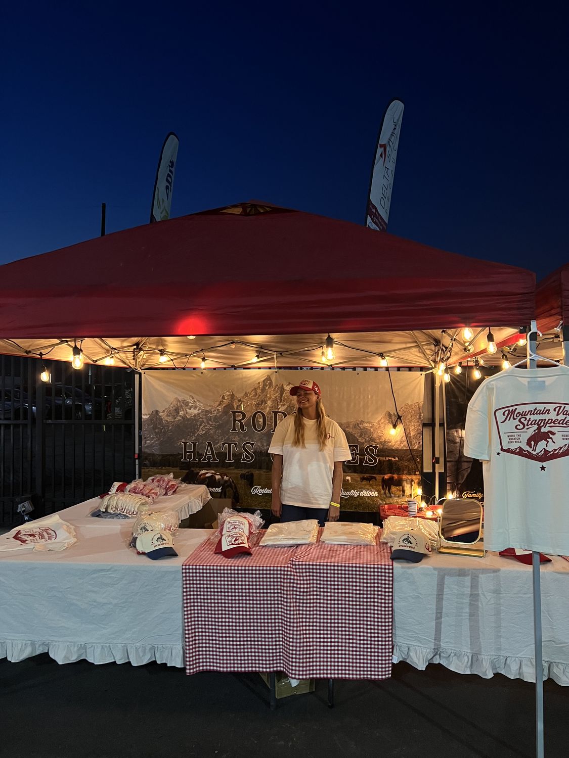 The Loud Face booth lit up at blue hour with Mountain Valley Stampede hats and tees on the table