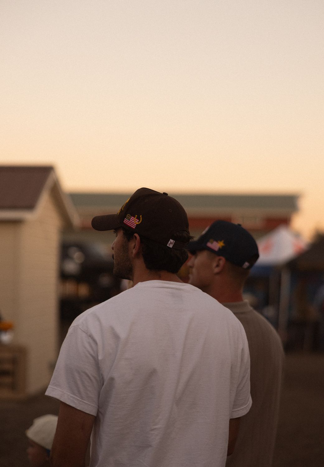 Two men in custom rodeo caps at the fairgrounds at sunset