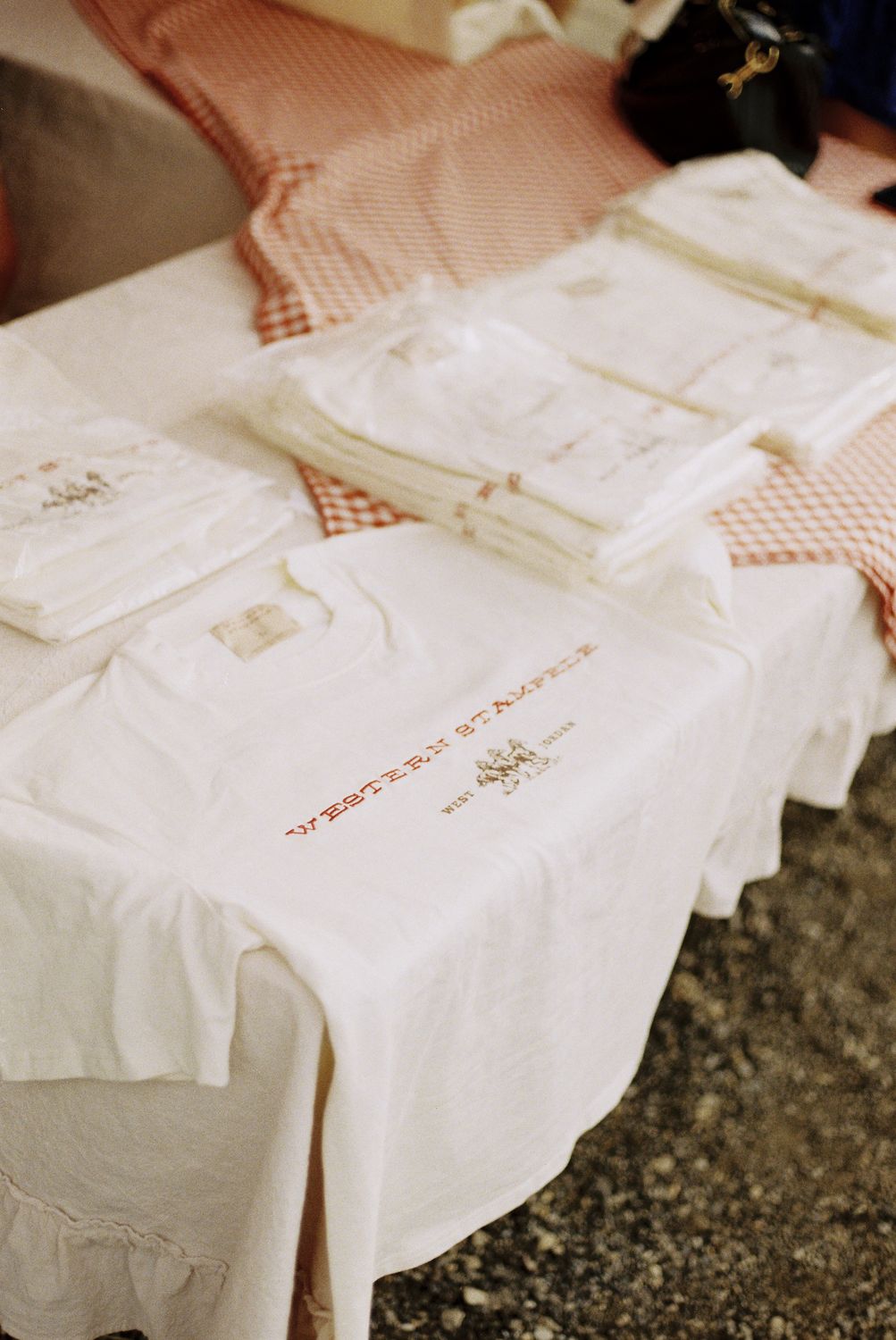 Folded Western Stampede tees stacked on the gingham booth table