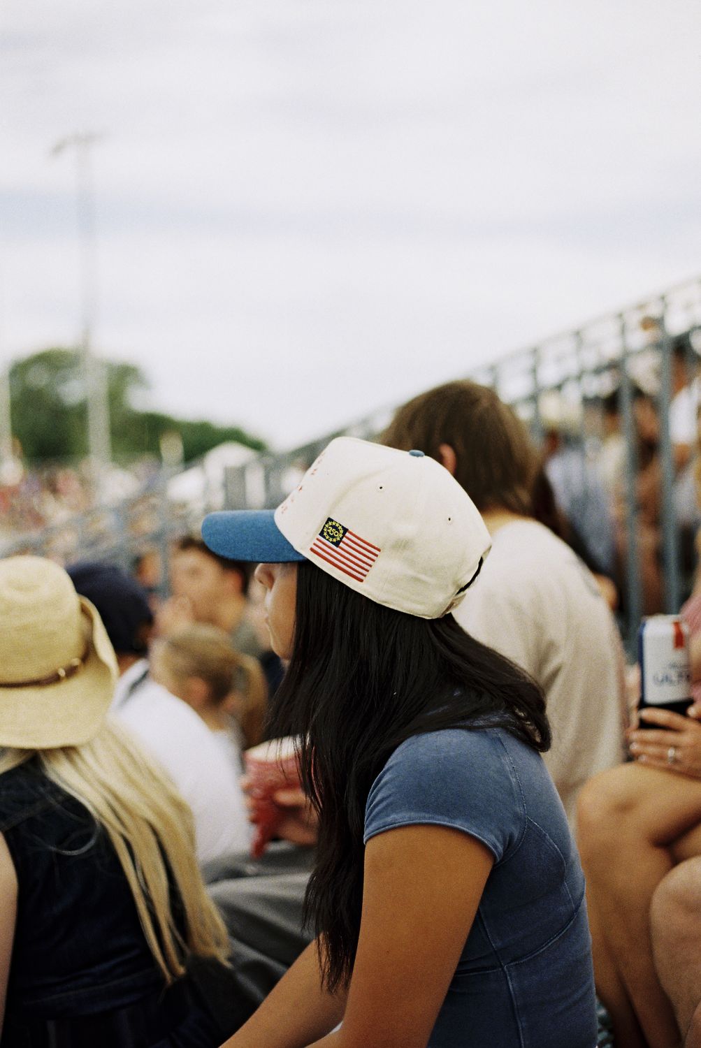 Fan in the stands wearing a cream flag-patch rodeo cap