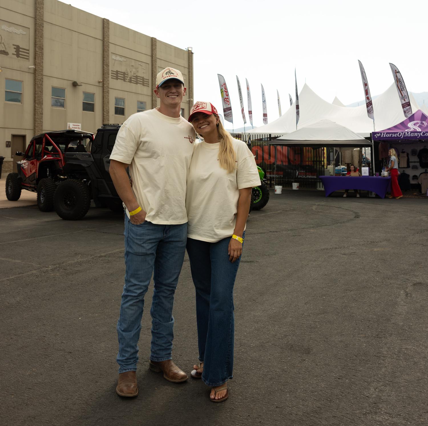 Couple in matching Mountain Valley Stampede tees and caps at the rodeo grounds