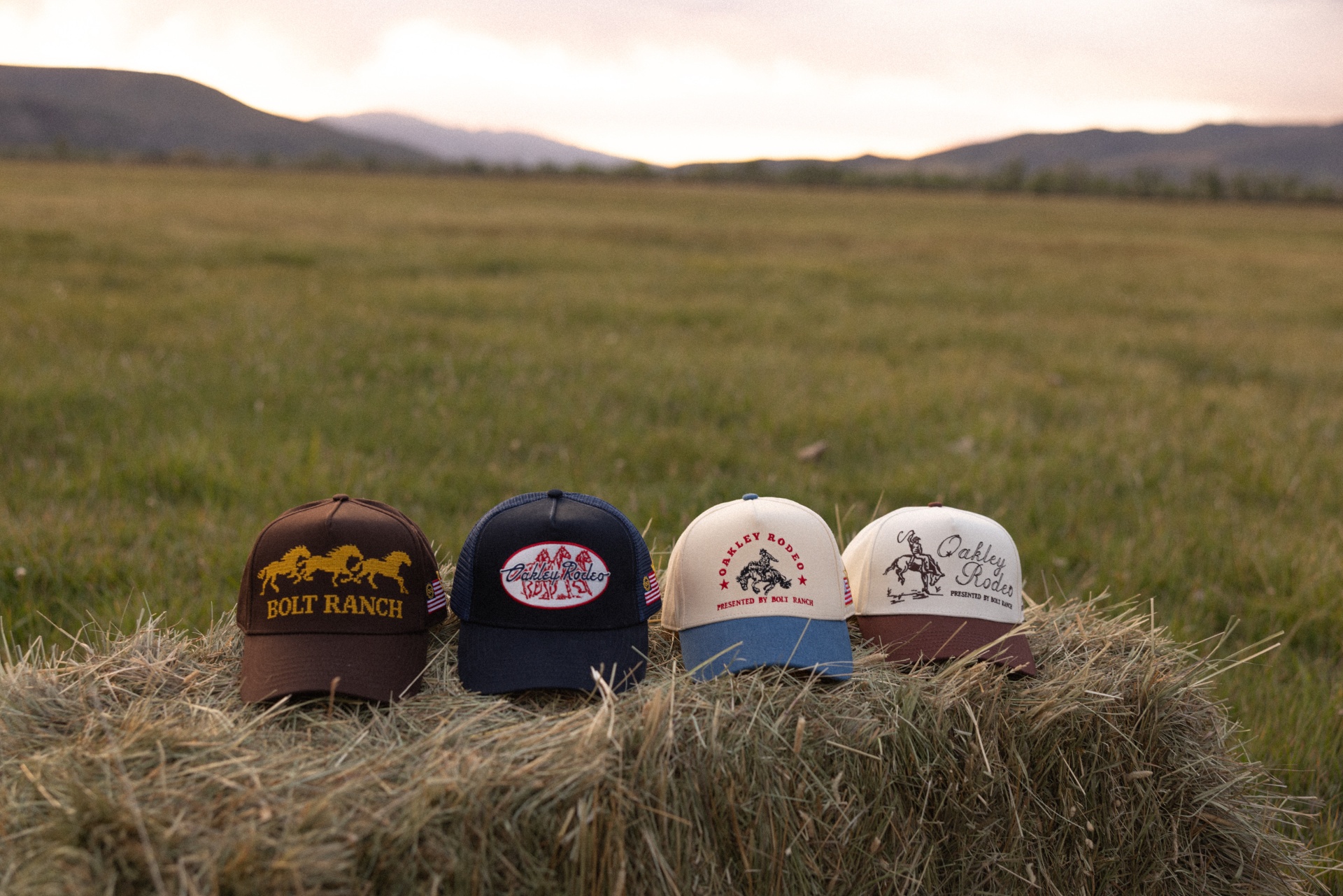 Four Bolt Ranch and Oakley Rodeo hats displayed on a hay bale at sunset