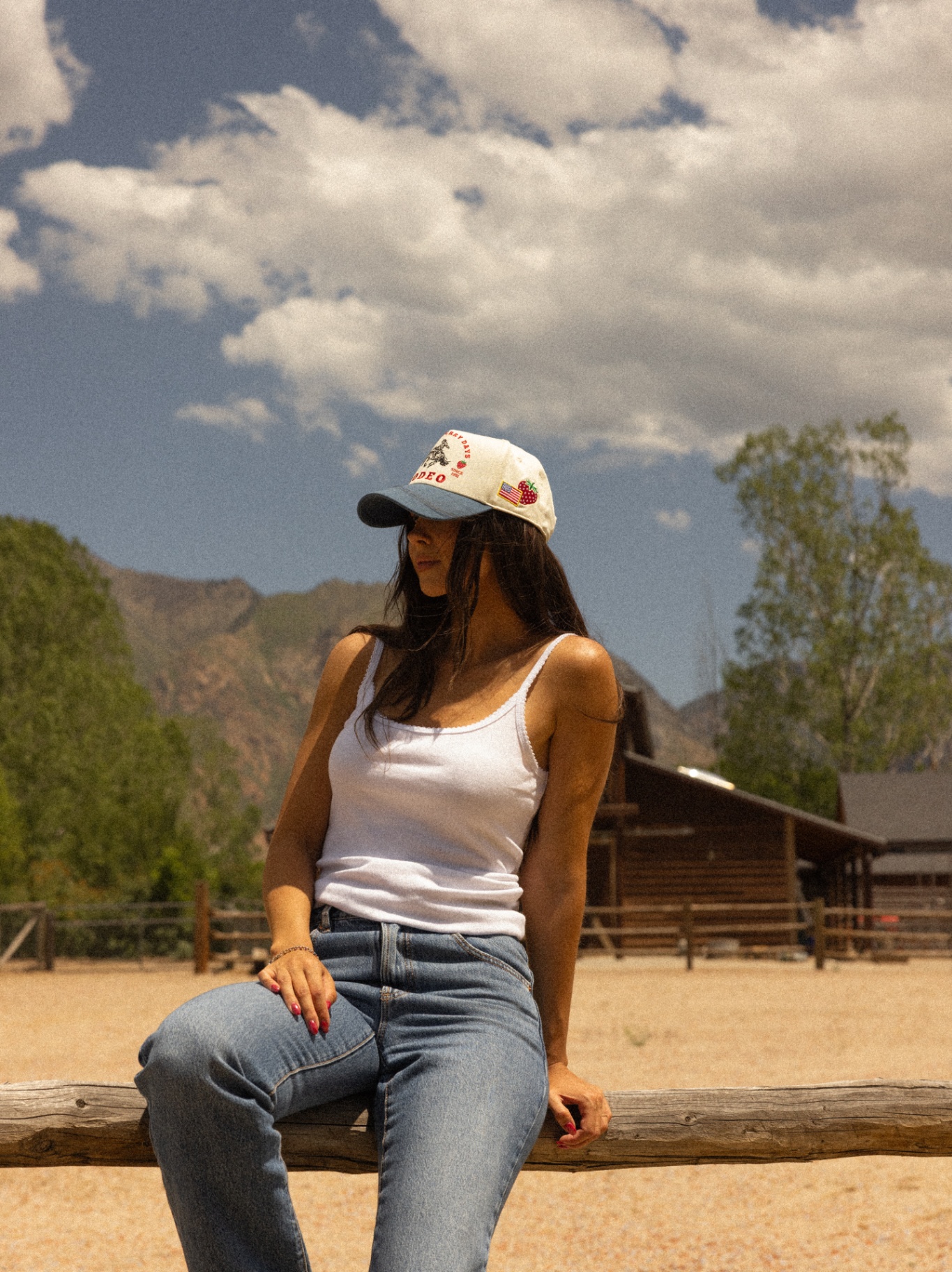 Model in denim and a Strawberry Days Rodeo cap seated outdoors with mountains behind